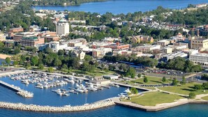 Un port de plaisance où sont amarrés des bateaux, entouré d’un mélange de bâtiments commerciaux et d’espaces verts.