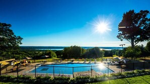 Une piscine avec vue sur l’océan, entourée d’une clôture et de verdure.