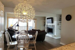 A dining area with a chandelier, a fireplace, and a television on the wall. - Bellaire, MI 2Bed, 3Bath Condo Shanty Creek-Winter Fun-World Class Golf Sleeps 8 (Bellaire)