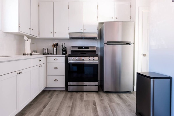 A modern kitchen with white cabinets, a stainless steel oven, a refrigerator, and a wooden floor.