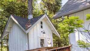 Un bâtiment blanc doté d’une terrasse en bois et d’une cheminée, entouré d’arbres.