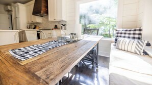 Une cuisine avec une table en bois, des placards blancs et une fenêtre donnant sur un espace verdoyant.
