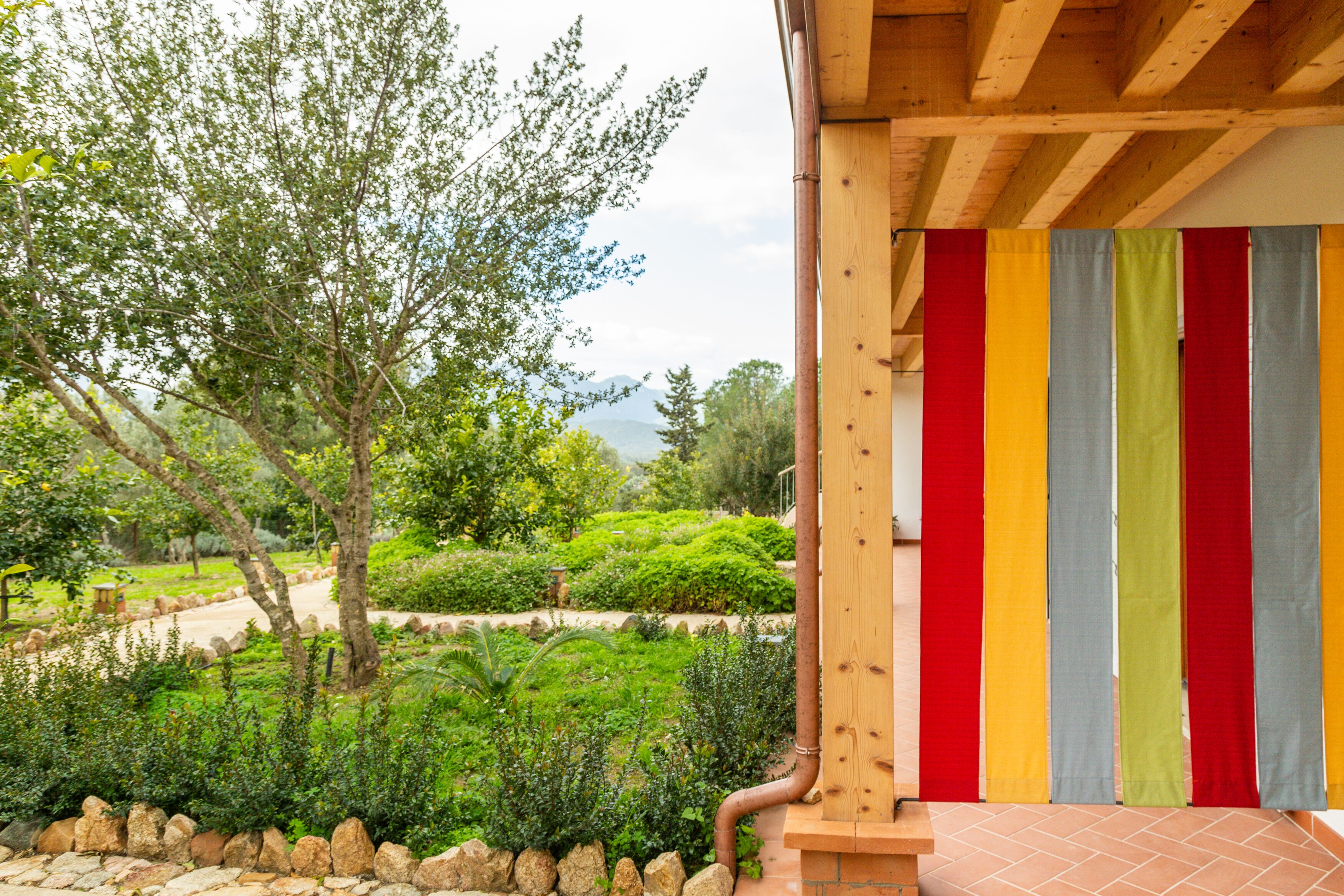Eine Holzhütte mit einem farbenfrohen, gestreiften Vorhang, einem Kiesweg und üppigem Grün.