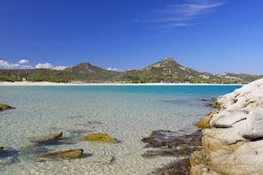 A coastal beach with clear turquoise waters, rocky shoreline, and a mountain in the background. - Domu Bresca (Muravera)