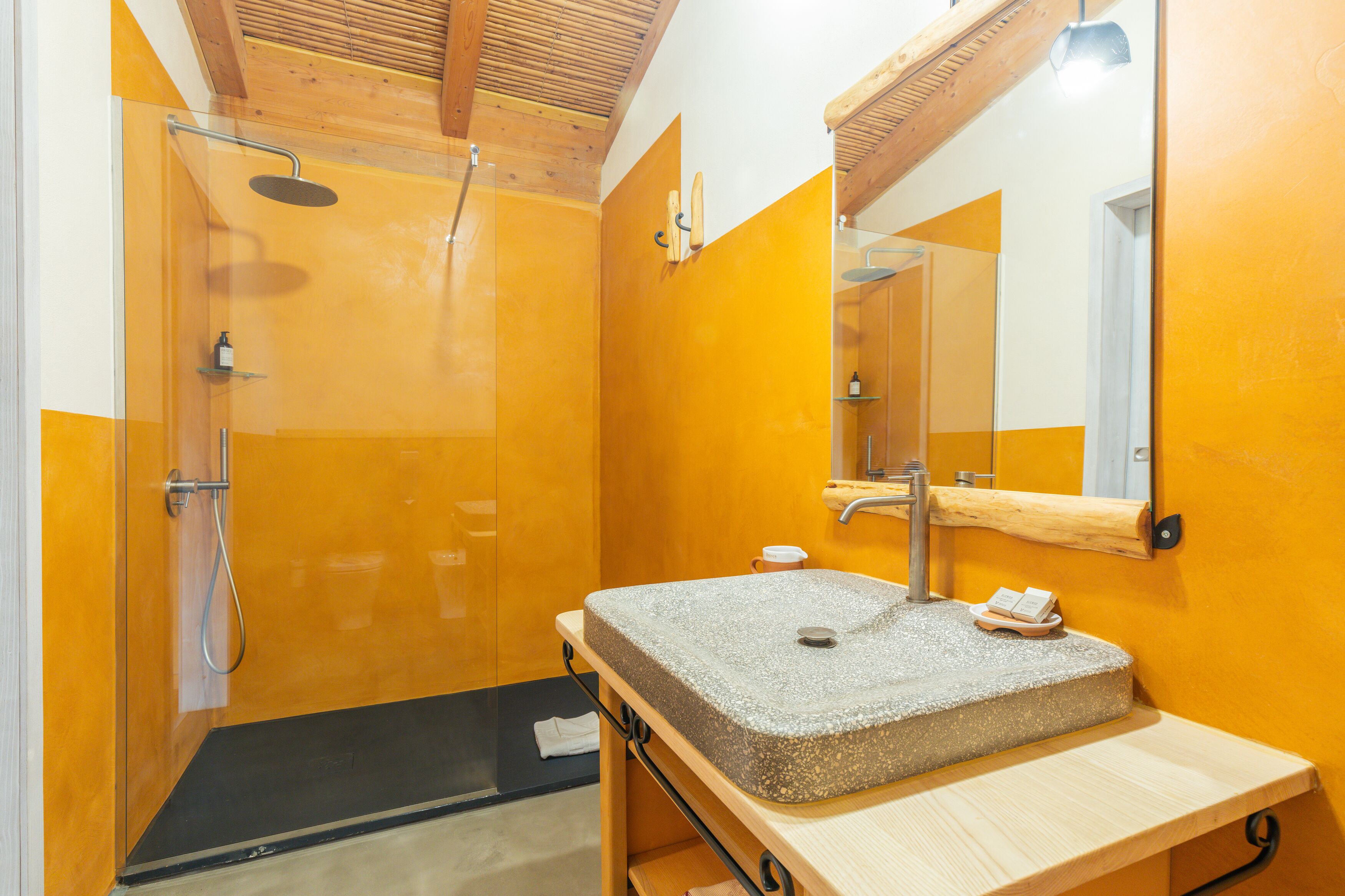 Ein modernes Badezimmer mit einer gläsernen Duschkabine, einem hölzernen Waschtisch mit Steinbecken und einem großen Spiegel.