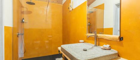 Ein modernes Badezimmer mit einer gläsernen Duschkabine, einem hölzernen Waschtisch mit Steinbecken und einem großen Spiegel.