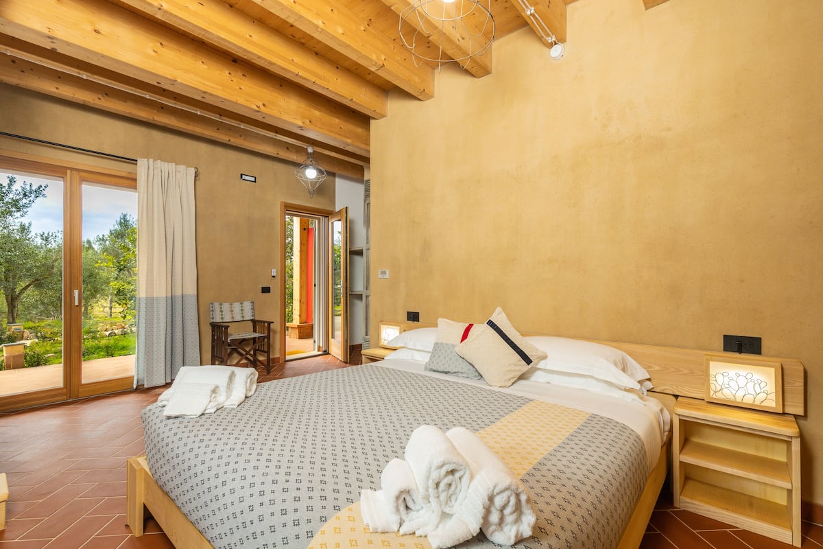 A spacious bedroom with a large bed, a wooden nightstand, and a view of a garden through a sliding glass door.
