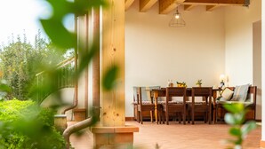 Una escalera de madera conduce a un comedor con una mesa y sillas, rodeado de follaje.