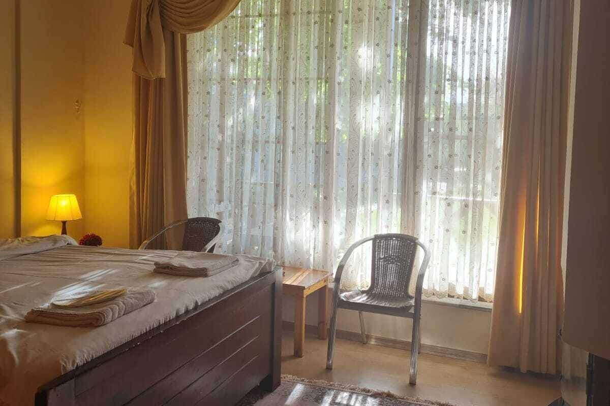 A hotel room with a bed, a chair, a table, and a large window with curtains.