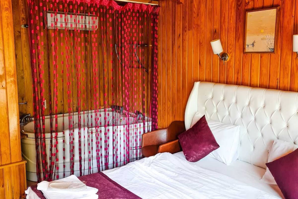 A wooden cabin bedroom with a large bed, a headboard, and a window with a view of the outdoors.