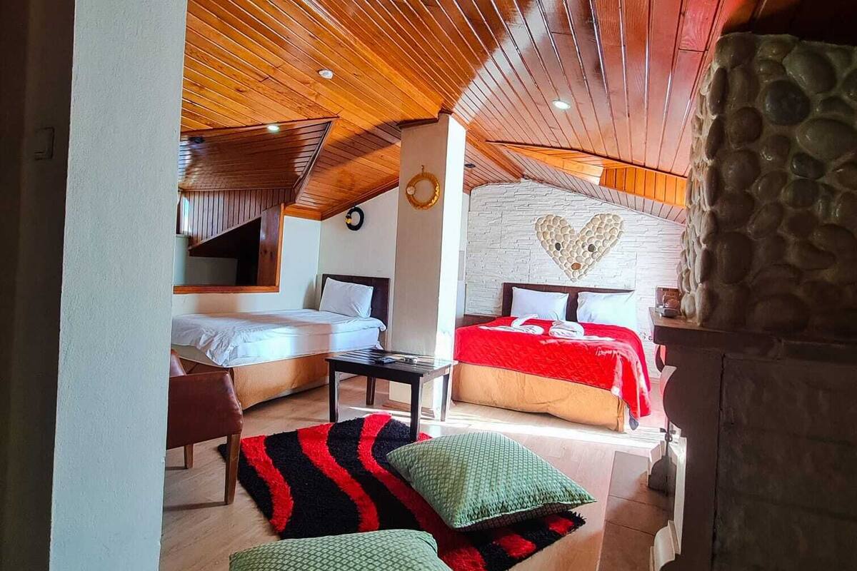A cozy room with a sloped ceiling, a stone wall with a heart design, two beds with red and white bedding, and a wooden floor.