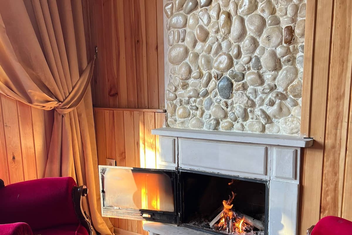 A cozy room with a stone wall, a fireplace, and two red velvet chairs.