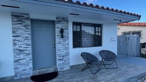 Une maison moderne avec un toit en tuiles, une façade en pierre et un porche à l’avant, agrémenté de deux chaises.
