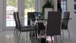 Un espace repas moderne avec une table et des chaises en verre, une plante en pot et une grande fenêtre donnant sur un paysage verdoyant.