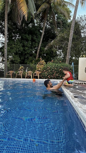 A swimming pool with tiled edges and a child playing near the edge.