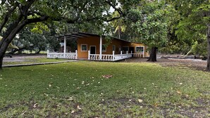 A yellow building with a white porch and a covered area, surrounded by trees and grass. - Paradise Bay (Puerto El Triunfo)