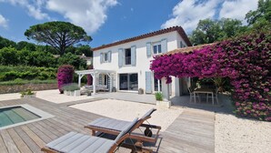 Une maison à deux étages avec un patio, une piscine et un jardin agrémenté de fleurs violettes.