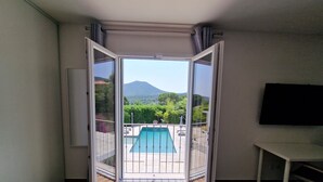 Un balcon ouvert donnant sur une piscine, un téléviseur fixé au mur et une vue sur la verdure et les collines.