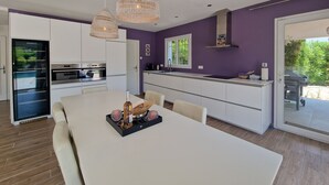 Une cuisine moderne avec des meubles blancs, une table à manger et des luminaires suspendus.