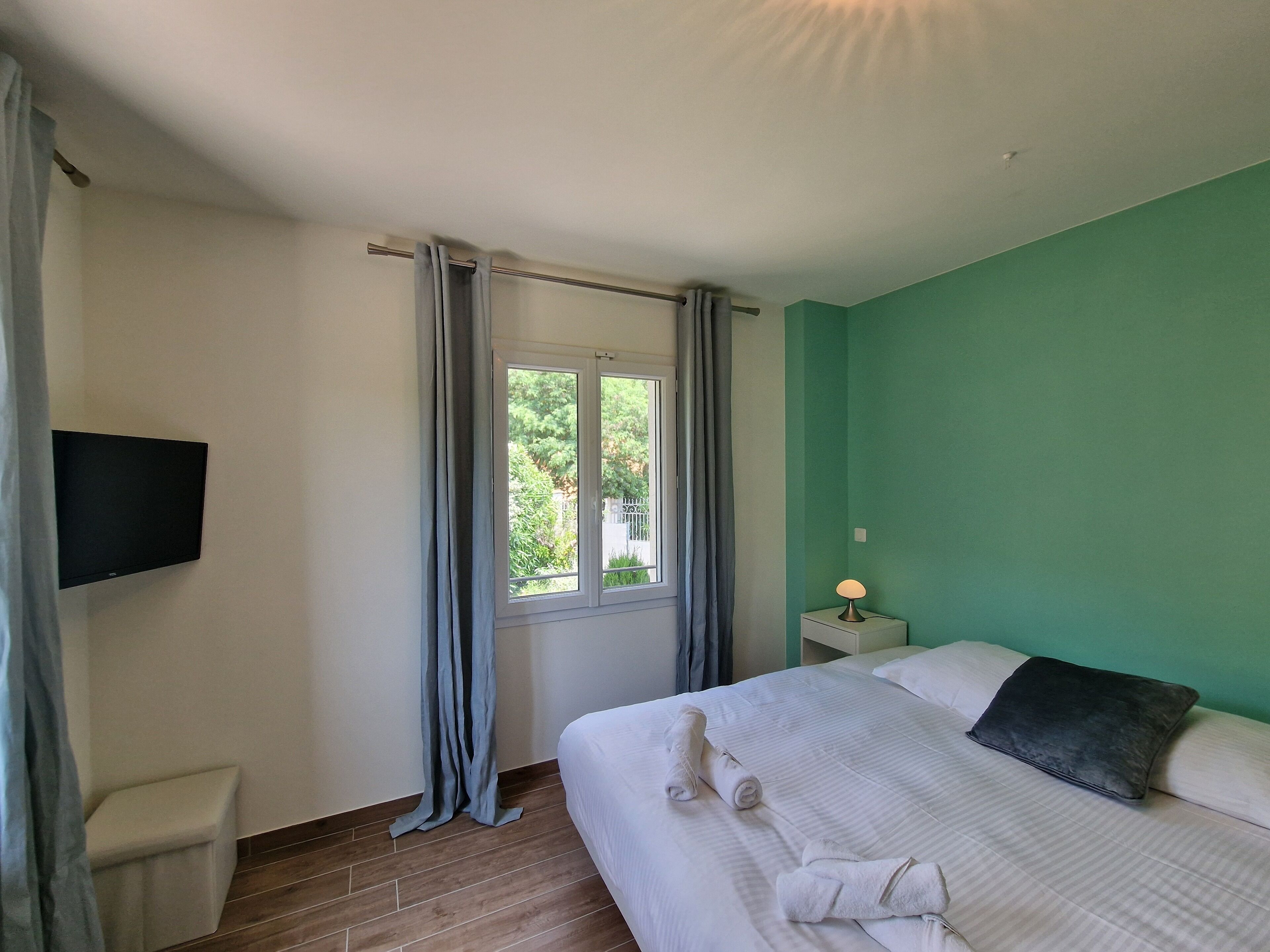 A hotel room with a bed, a nightstand, a lamp, a TV, and a window with curtains.