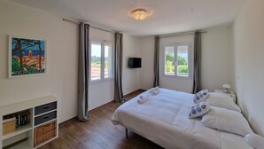 Une chambre à coucher avec un lit, deux fenêtres, un tableau, une télévision et une table de chevet.