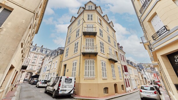 Una calle estrecha bordeada de edificios de varios pisos, con balcones y contraventanas.