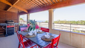 Un espace extérieur abrité, aménagé pour les repas, avec une table pour quatre personnes, un barbecue et une vue sur la plage.