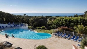Une piscine avec des chaises bleues et vue sur la mer.