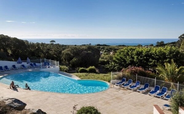 A pool with blue chairs and a view of the sea.
