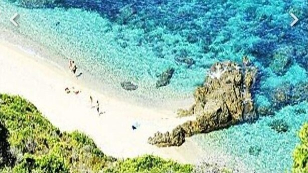 Une plage à l’eau turquoise et limpide, bordée d’un rivage sablonneux et ponctuée de formations rocheuses.