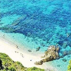 Ein Strand mit klarem türkisblauem Wasser, einem sandigen Ufer und Felsen.