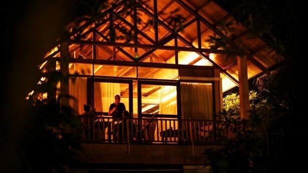 Une structure en bois dotée d’un balcon, de grandes fenêtres et d’une personne se tenant sur le balcon.