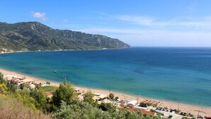 Eine Küstenansicht mit Strand, klarem blauen Meer und einem Berg im Hintergrund.