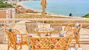 Eine Terrasse mit Korbmöbeln und einem Tisch, mit Blick auf Strand und Berge.