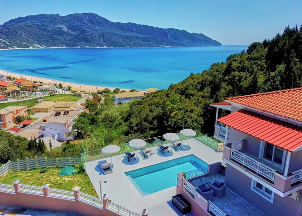 Un resort con piscina, poltrone relax e vista sul mare e sulle montagne.