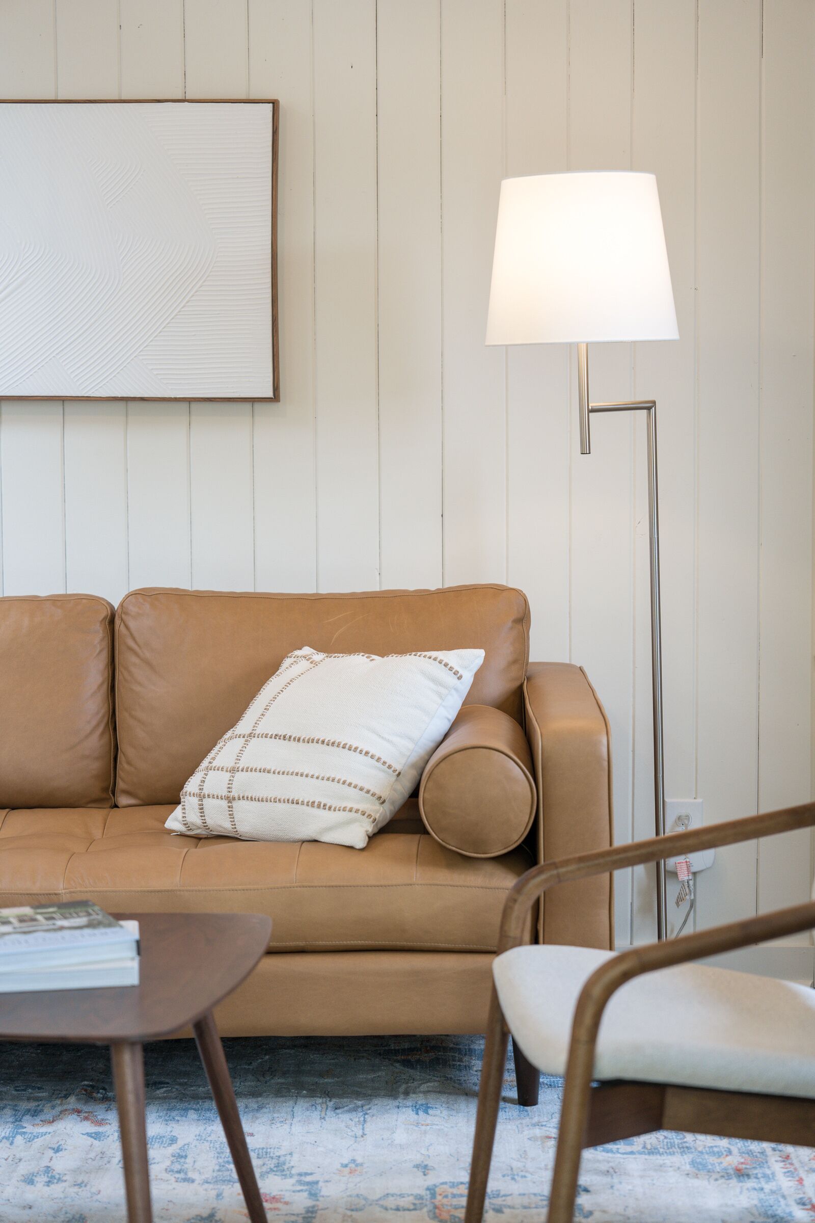 A modern living room with a brown leather sofa, a white pillow, a floor lamp, and a small table.