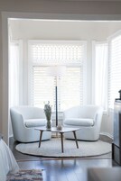 Una sala de estar con dos sillones blancos, una mesa redonda de centro, una lámpara de pie y un jarrón decorativo.