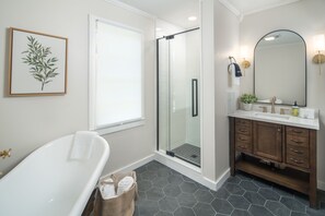 A bathroom with a freestanding bathtub, a glass-enclosed shower, a wooden vanity with a large mirror, and a framed botanical print on the wall. - The Victorian Inn Blowing Rock (Blowing Rock)