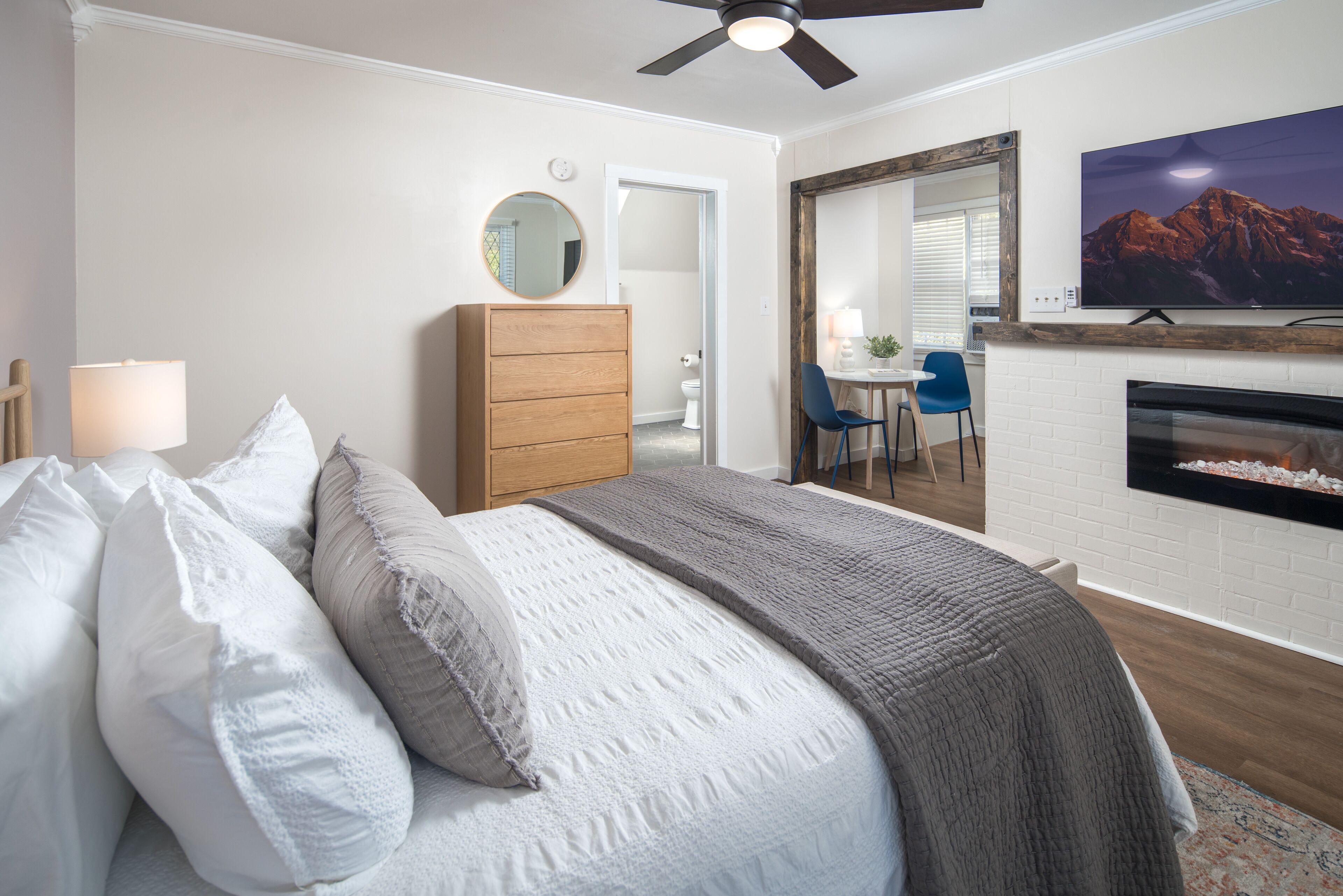 A bedroom with a bed, dresser, TV, fireplace, and a view of the bathroom.