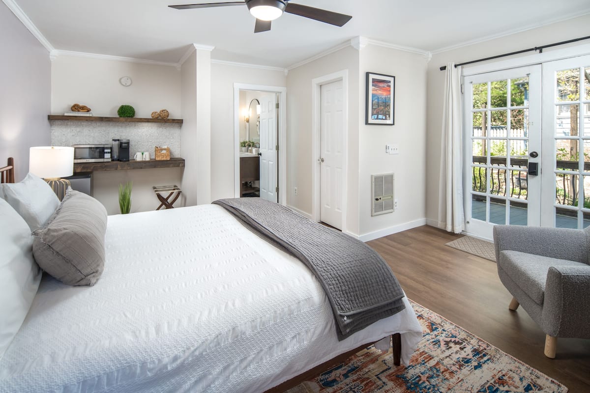 A bedroom with a bed, a chair, a desk, and a kitchenette.