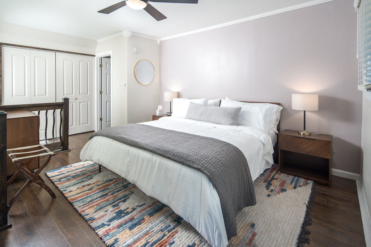 A bedroom with a bed, nightstands, a ceiling fan, and a door leading to another room.