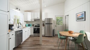 A modern kitchen with white cabinetry, stainless steel appliances, and a wooden dining table with green chairs. - The Victorian Inn Blowing Rock (Blowing Rock)