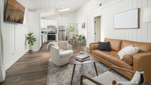 A spacious living area with a brown leather sofa, a white armchair, and a coffee table. A kitchen is visible in the background with white cabinetry and stainless steel appliances. - The Victorian Inn Blowing Rock (Blowing Rock)