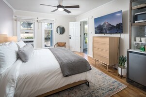 A bedroom with a bed, a ceiling fan, a dresser, a TV, and a view of the outdoors.