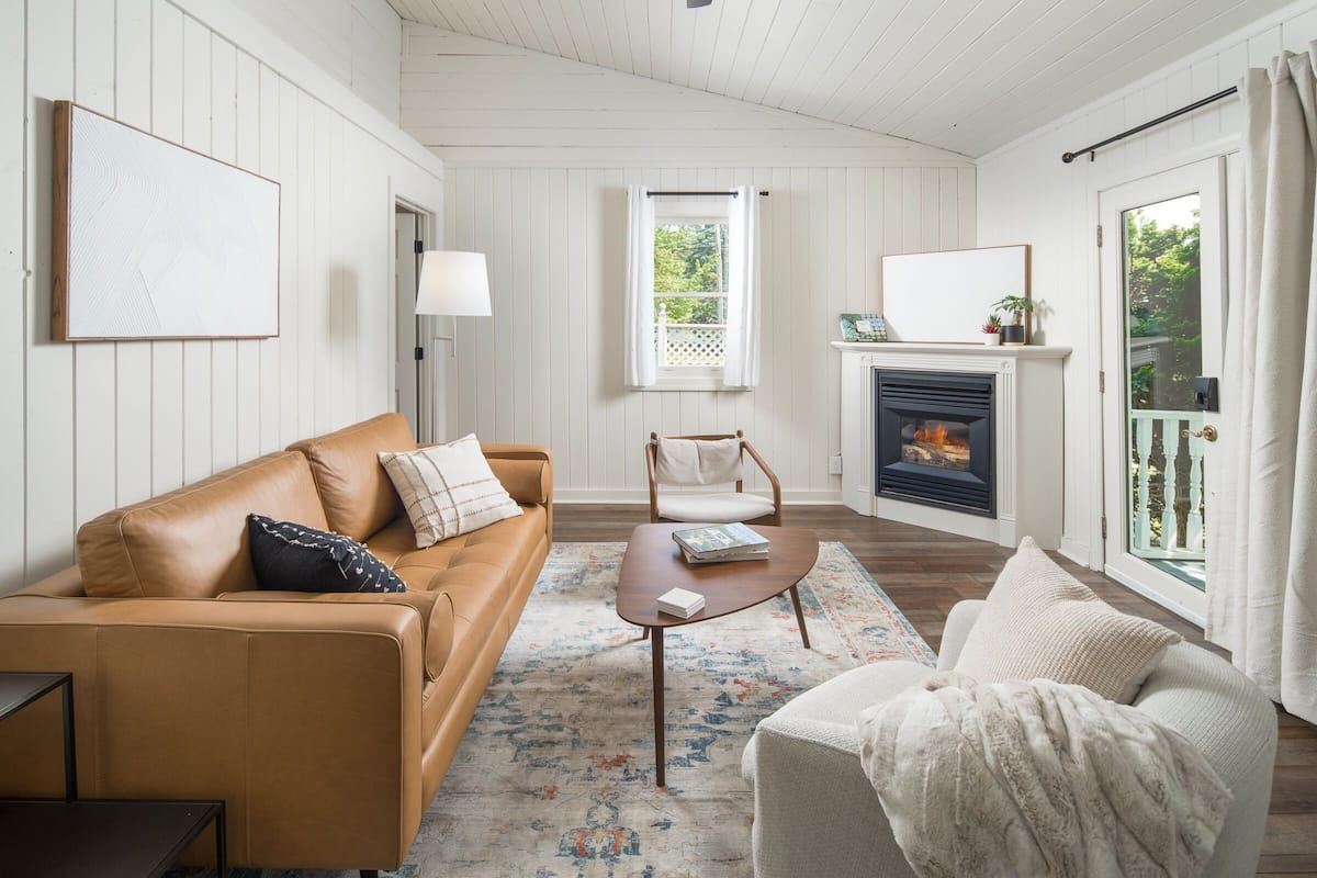 A living room with a brown leather sofa, a white armchair, a wooden coffee table, and a fireplace.