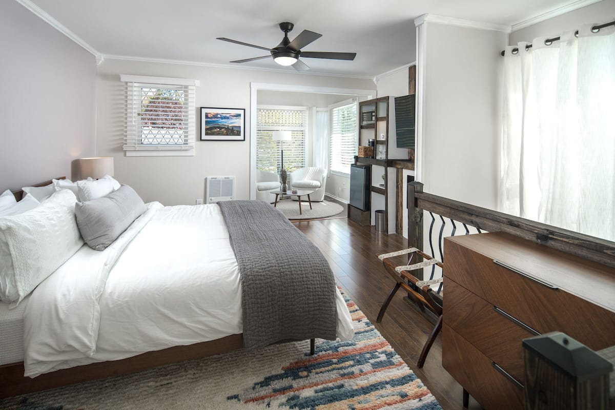 A bedroom with a bed, a desk, a chair, a ceiling fan, and a window with blinds.