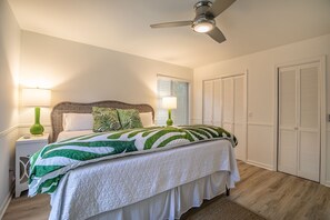 Une chambre à coucher avec un lit, deux lampes de chevet, un ventilateur de plafond et des armoires blanches.