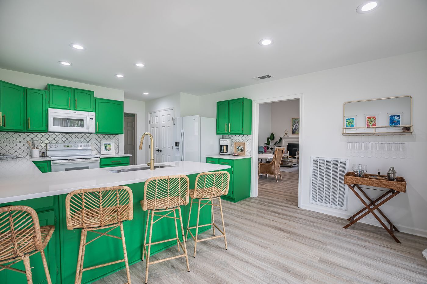 A modern kitchen with green cabinets, white countertops, and a central island with bar stools.