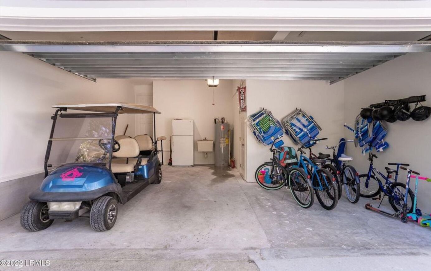 A garage with a golf cart, bicycles, and a refrigerator.