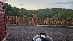 Eine Kiesterrasse im Vordergrund mit einem schwarzen Grill und im Hintergrund ein Holzzaun.
